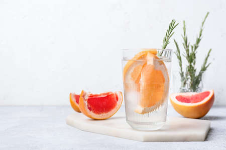 Glass of cold gin tonic and grapefruit slices on light background