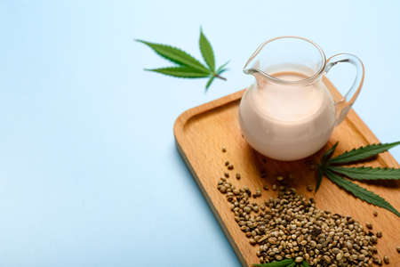 Wooden board with pitcher of hemp milk, seeds and leaves on blue backgroundの写真素材