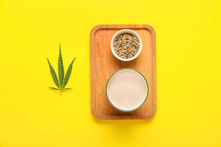 Wooden board with glass of hemp milk and seeds on yellow backgroundの写真素材