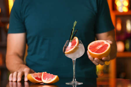Male bartender with glass of grapefruit gin and tonic in bar