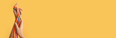 Female hands holding rainbow ribbon on orange background with space for text. LGBT concept