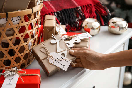 Christmas advent calendar with gift boxes in basket and woman holding present, closeup