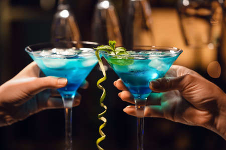 Women clinking glasses of Blue cocktail on table in barの写真素材
