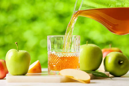 Pouring of apple juice from jug into glass on table outdoorsの写真素材