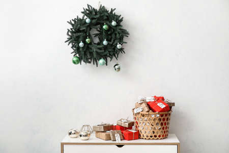 Advent calendar with gift boxes in basket on chest of drawers and Christmas wreath on white wallの写真素材