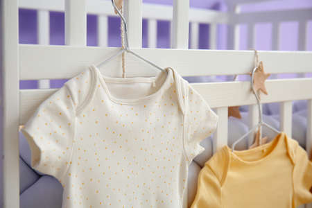 Baby bodysuits hanging on crib in children's bedroom, closeupの写真素材