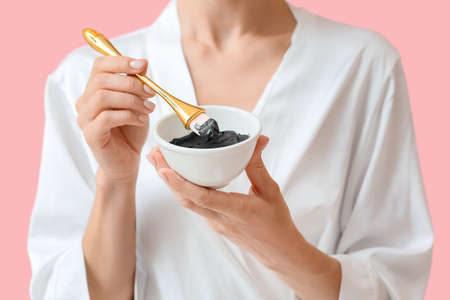 Young woman with activated charcoal mask against color background, closeup