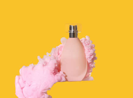 Perfume bottle in pink smoke on yellow backgroundの写真素材