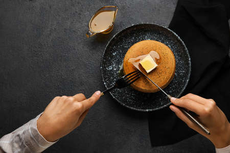 Woman eating tasty pancakes with honey on dark background