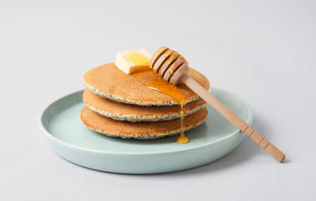 Plate of tasty pancakes with honey and butter on light background