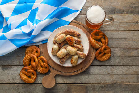 Mug of cold beer, board with Bavarian sausages and snacks on wooden background. Oktoberfest celebrationの写真素材