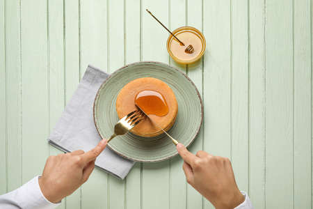 Woman eating tasty pancakes with honey on color wooden backgroundの写真素材
