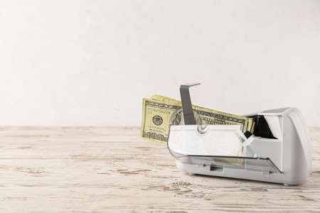 Dollars in currency counting machine on wooden table against light background