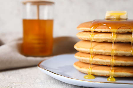 Plate of tasty pancakes with honey and butter on light background, closeup
