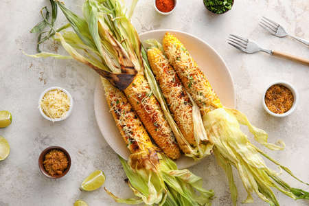 Plate with delicious Elote Mexican Street Corn and spices on light background