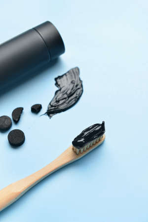 Tube with activated carbon toothpaste, toothbrush and pills on blue background, closeup
