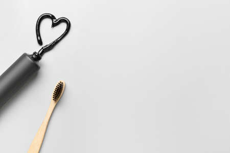 Toothbrush and tube with activated carbon toothpaste on light background, closeup