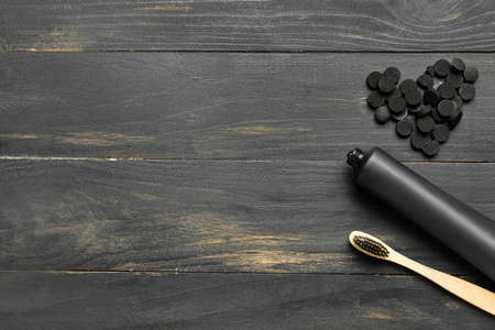 Tube with activated carbon toothpaste, toothbrush and heart made of pills on dark wooden background