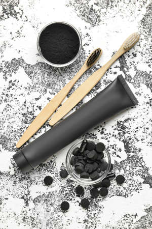 Toothpaste tube, bamboo toothbrushes, bowls with activated charcoal tooth powder and pills on grunge backgroundの写真素材