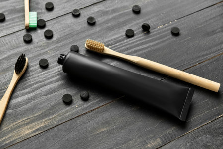 Tube with activated carbon toothpaste, bamboo toothbrushes and pills on dark wooden background,...