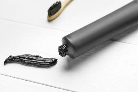 Tube with activated carbon toothpaste on white wooden background, closeup