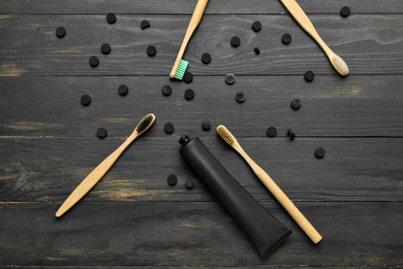 Tube with activated carbon toothpaste, bamboo toothbrushes and pills on dark wooden background
