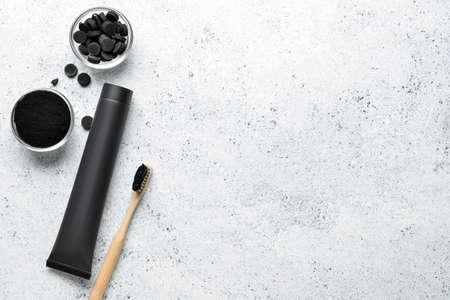 Toothpaste tube, bamboo toothbrush, bowls with activated charcoal tooth powder and pills on light...