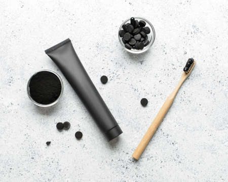 Bamboo toothbrush, toothpaste tube, bowls with activated charcoal tooth powder and pills on light...