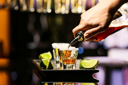 Bartender pouring tasty tequila into glasses at table in bar