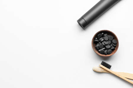 Tube with activated carbon toothpaste, bowl with pills and bamboo toothbrushes on white background,...
