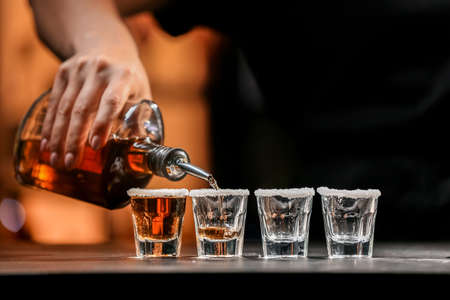 Bartender pouring tasty tequila into glasses at table in barの写真素材
