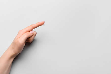 Female hand with gentle manicure pointing at something on gray backgroundの写真素材