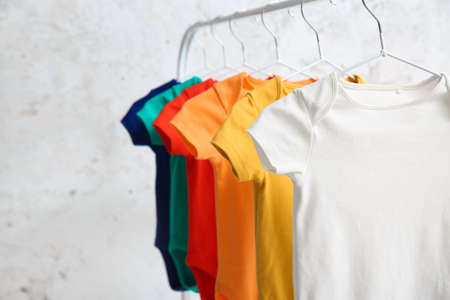Rack with colorful baby bodysuits near light wall, closeupの写真素材