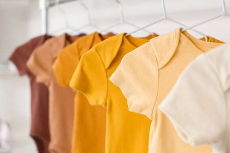 Baby bodysuits hanging near light wall in room, closeup