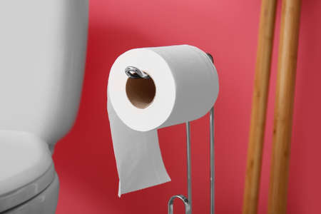 Holder with roll of toilet paper near pink wall, closeup