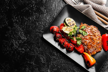 Plate with tasty pork steak and grilled vegetables on dark backgroundの写真素材