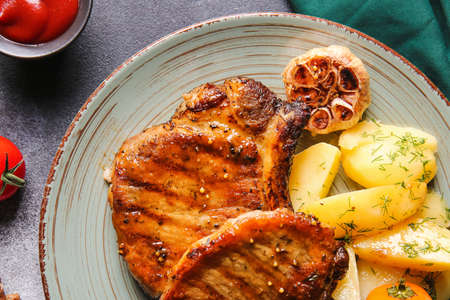 Plate with tasty pork steaks and vegetables on gray background, closeup