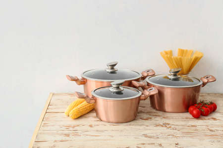 Copper cooking pots and raw food on wooden table against white background