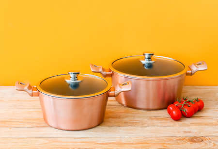 Copper cooking pots and tomatoes on wooden table against orange backgroundの写真素材