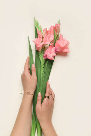 Female hands with gladiolus flowers on color backgroundの写真素材