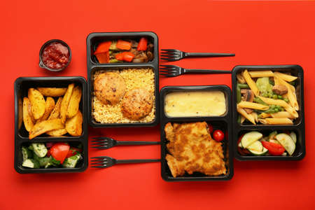 Lunch boxes with different tasty food and forks on color backgroundの写真素材