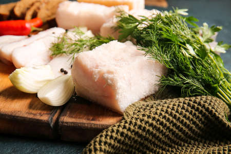 Wooden board with salted lard on dark background