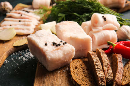 Wooden boards with salted lard and bread on dark background