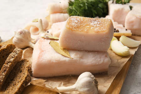 Wooden board with salted lard and bread on light backgroundの写真素材