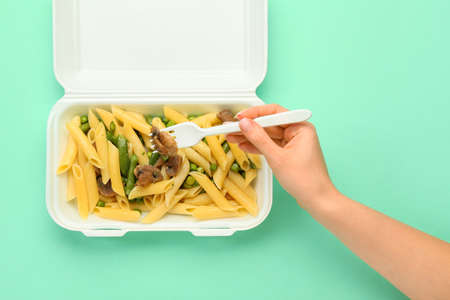 Woman taking pasta with vegetables from lunch box on color backgroundの写真素材