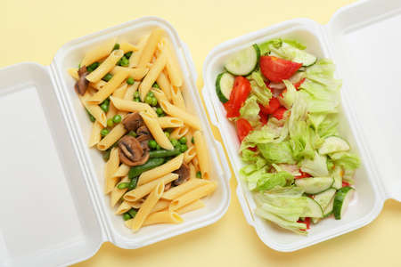 Delicious vegetable salad and pasta in containers on color background, closeupの写真素材