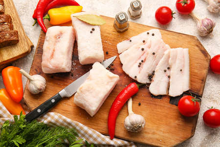 Wooden board with salted lard and fresh vegetables on light background