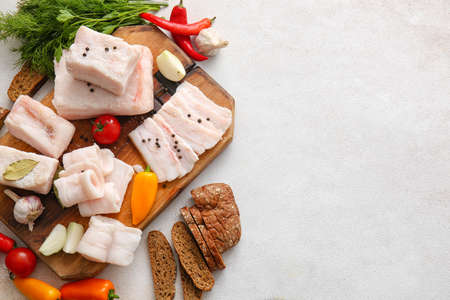 Wooden board with salted lard, bread and fresh vegetables on light background