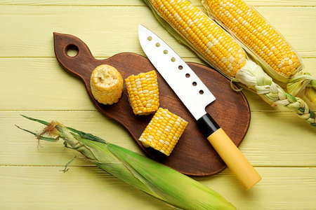 Board with fresh corn cobs and knife on color wooden backgroundの写真素材