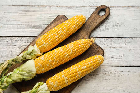 Board with fresh corn cobs on light wooden backgroundの写真素材